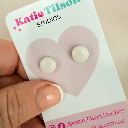White circular stud earrings on a Katie Tilson Studios card held by a hand.