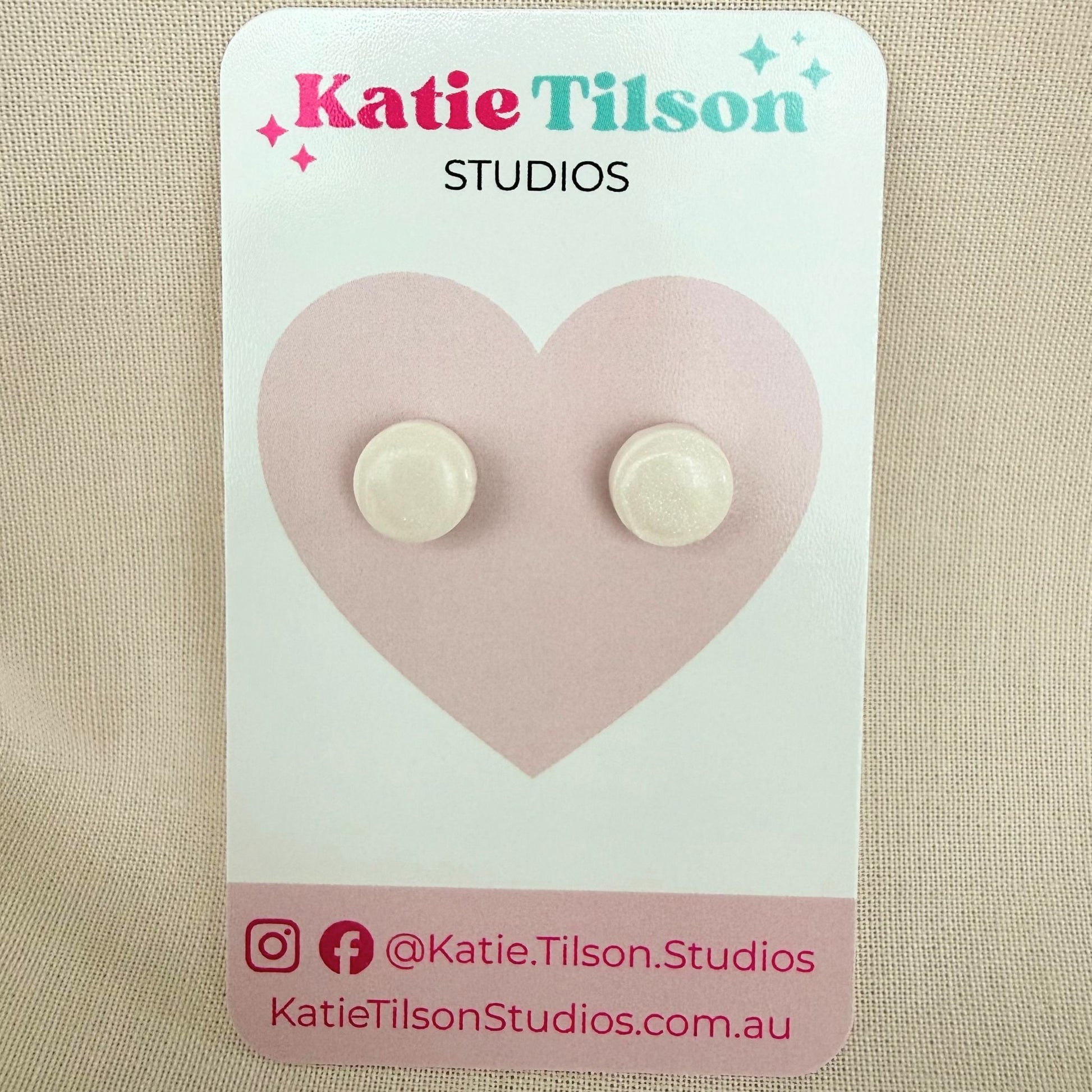 White circular stud earrings on a Katie Tilson Studios card against beige background.