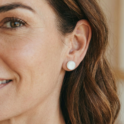 Close-up of a woman wearing white stud earrings with a glossy finish against a blurred background.