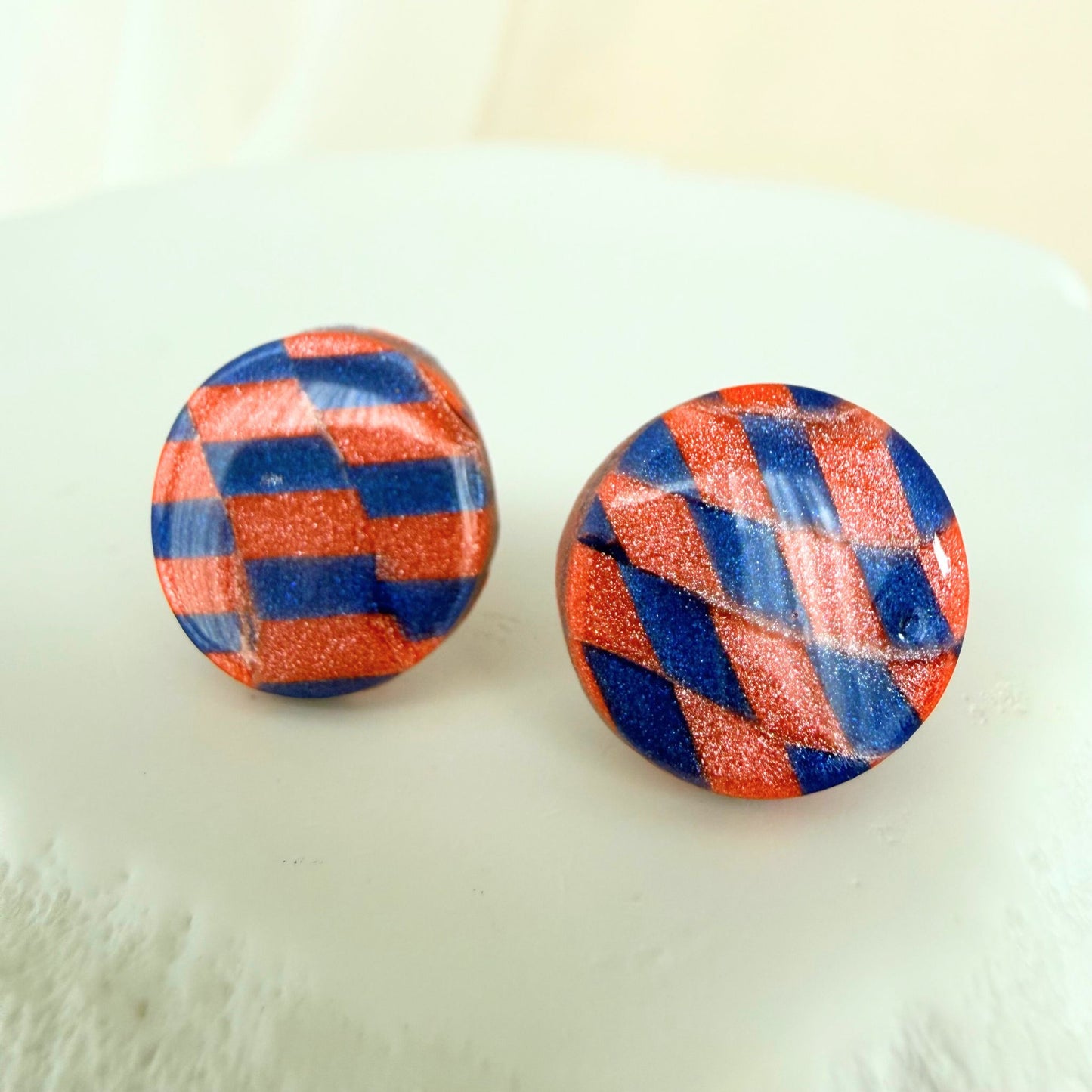 Pair of round stud earrings with cobalt blue and coral checkered pattern on a white surface.