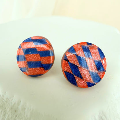 Pair of round stud earrings with cobalt blue and coral checkered pattern on a white surface.
