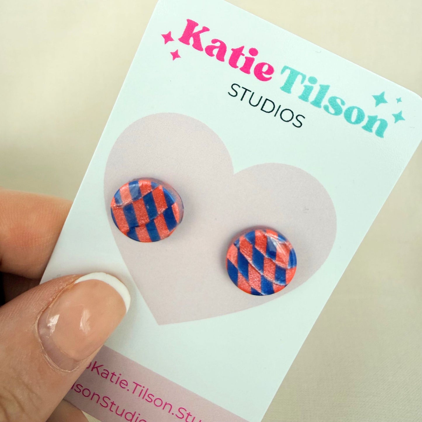 Colorful blue and coral checkered circular stud earrings on a Katie Tilson Studios card held by a hand.