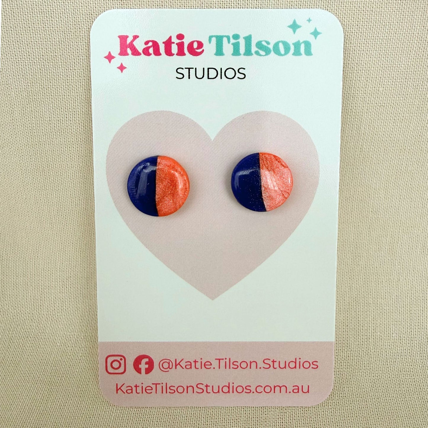 Cobalt blue and coral half and half  design circular stud earrings on a branded earring card against a beige background.