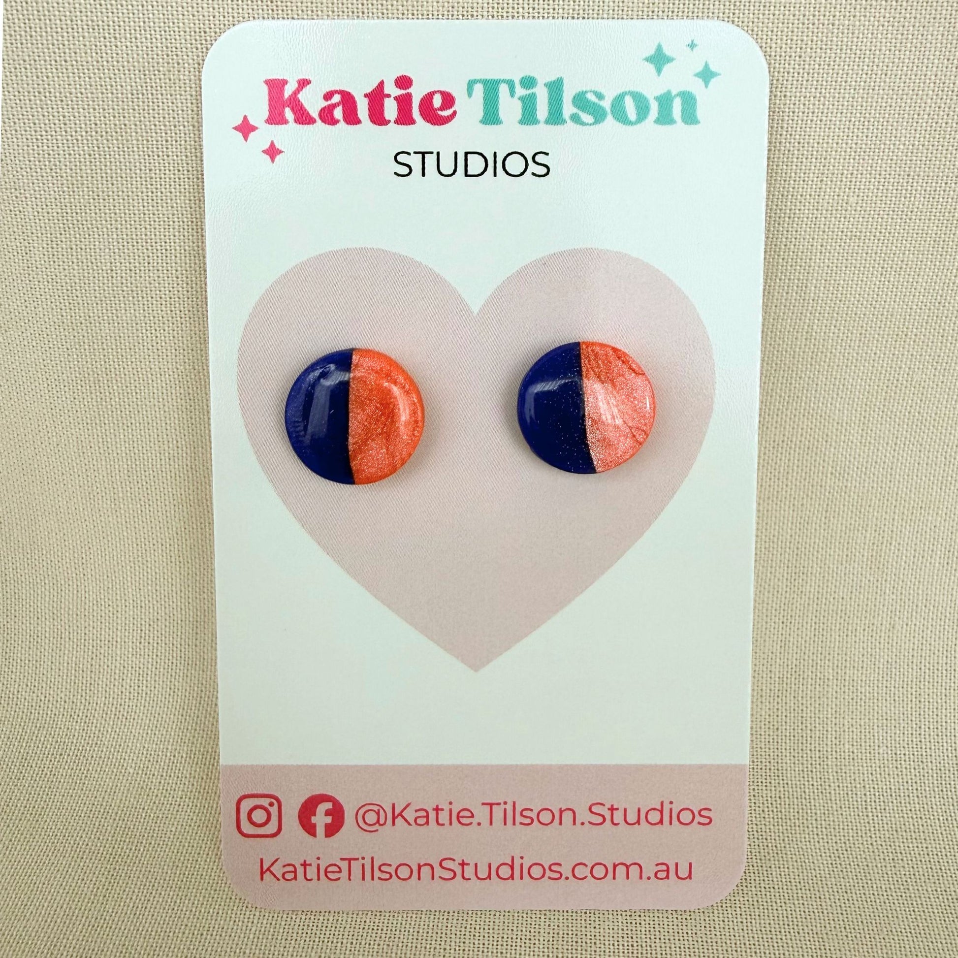 Cobalt blue and coral half and half  design circular stud earrings on a branded earring card against a beige background.