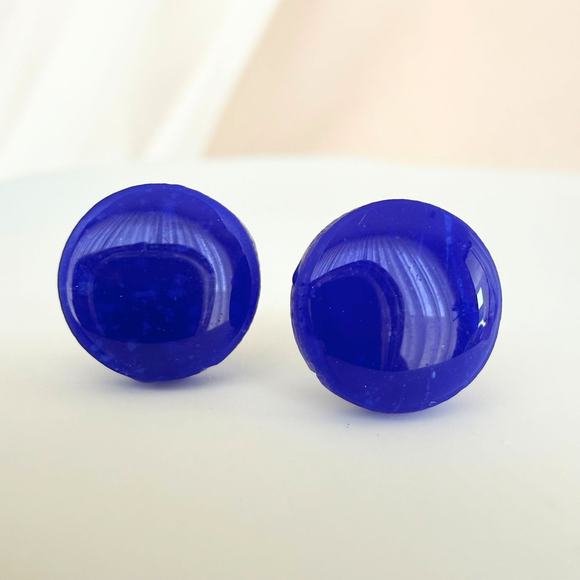 A pair of bright cobalt blue circle studs with a glossy resin finish resting on a white surface.