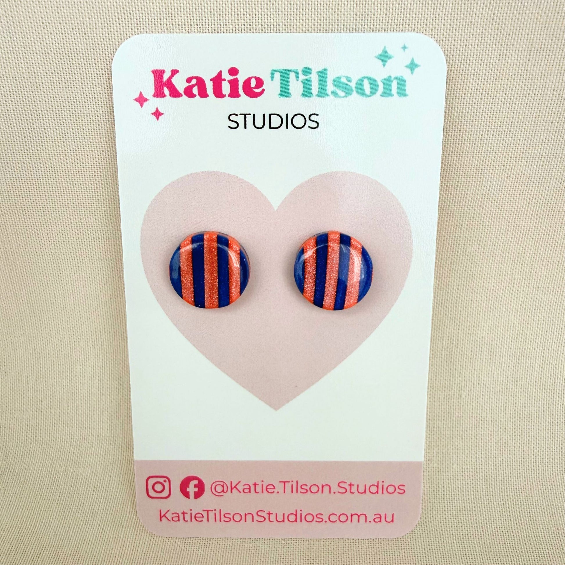 Cobalt blue and coral striped circular stud earrings on a Katie Tilson Studios card against a beige background.