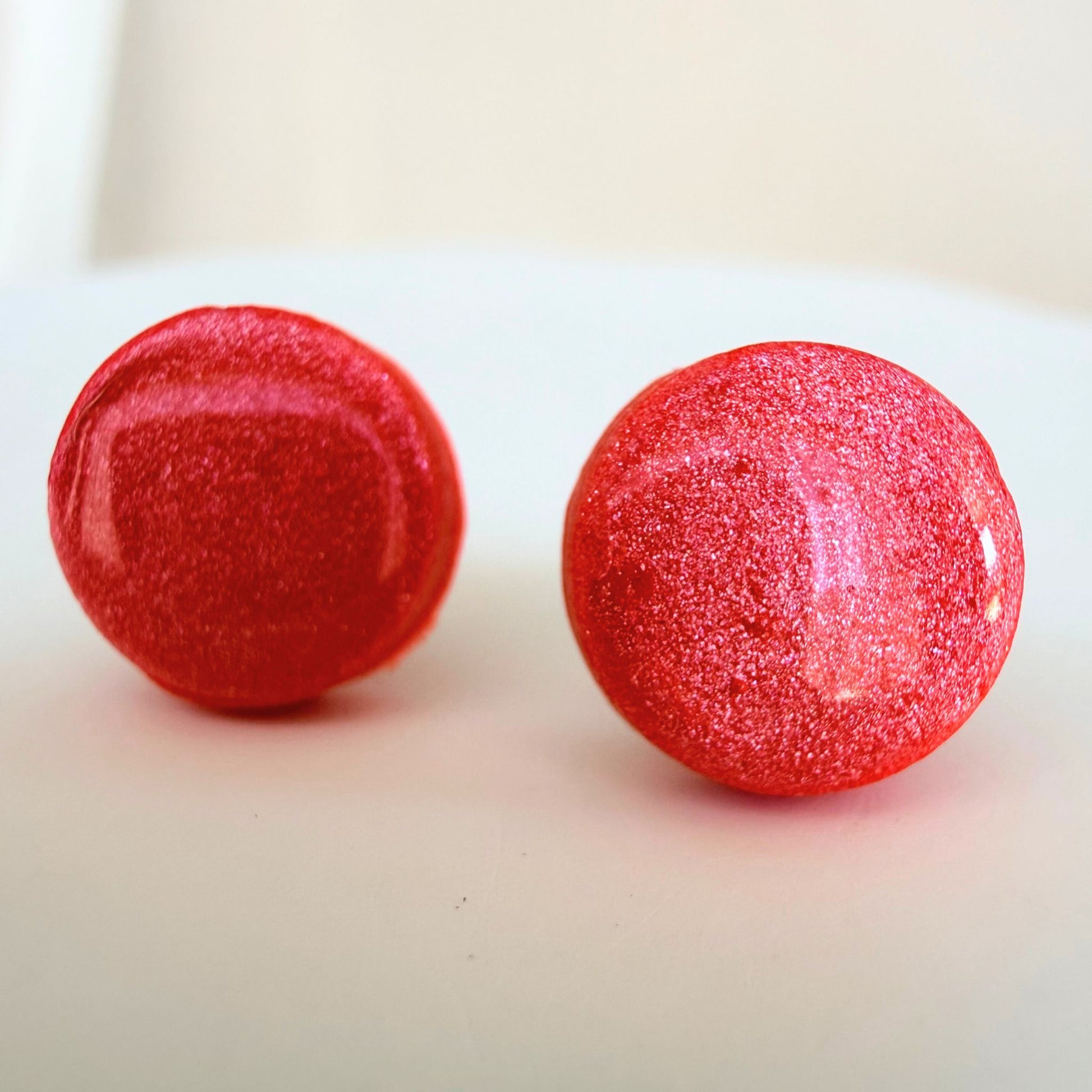 A pair of bright coral coloured circle studs with shimmer and glossy resin finish resting on a white surface.