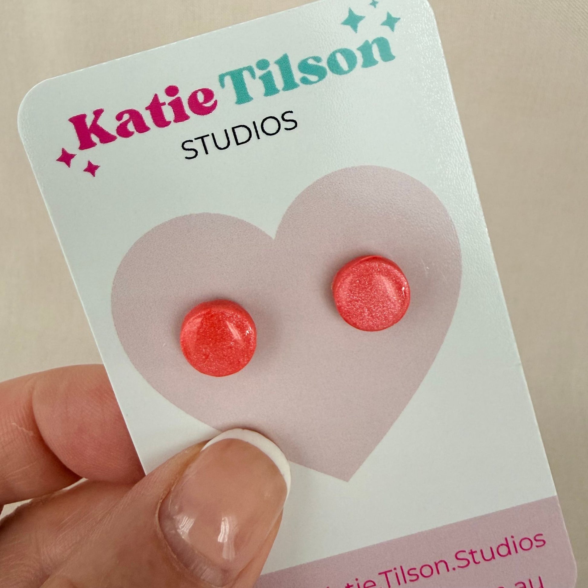 Coral colour round stud earrings on a Katie Tilson Studios card held by a hand.