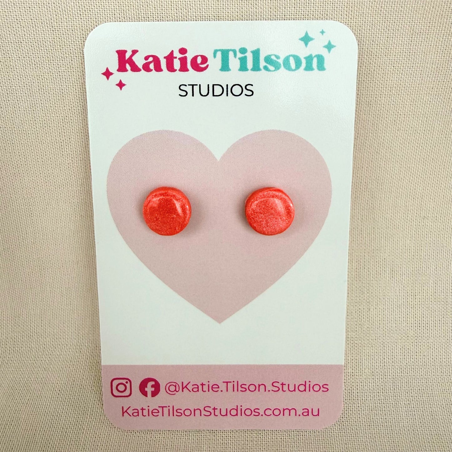 Coral colour round stud earrings on a Katie Tilson Studios branded earring card against a beige background.