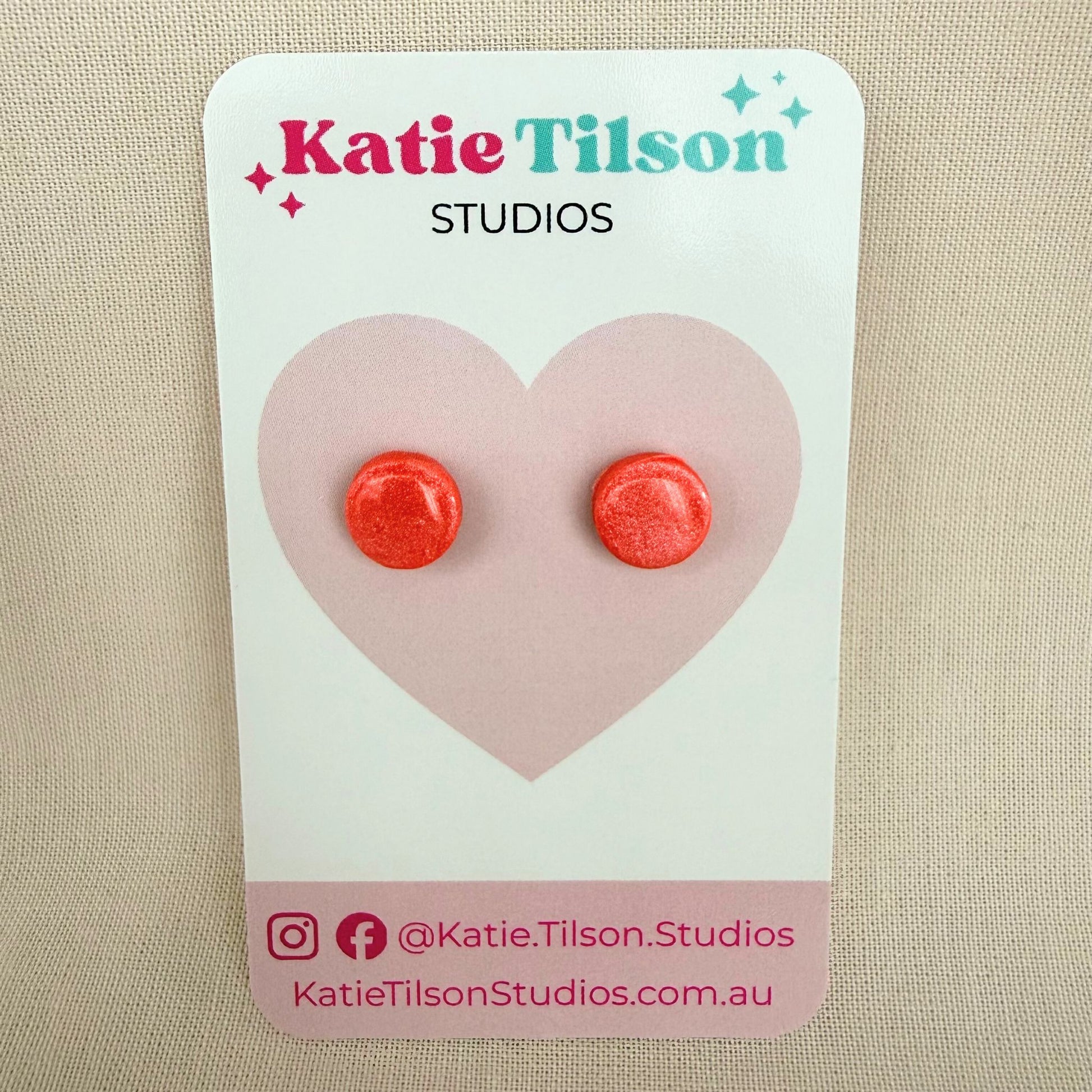 Coral colour round stud earrings on a Katie Tilson Studios branded earring card against a beige background.