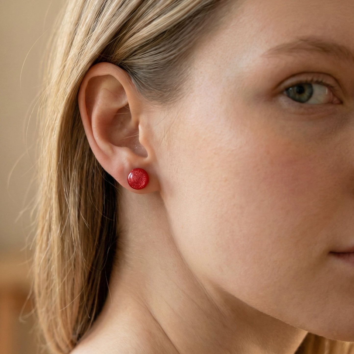 Close-up of a woman wearing round coral stud earrings with a glossy finish against a blurred background.