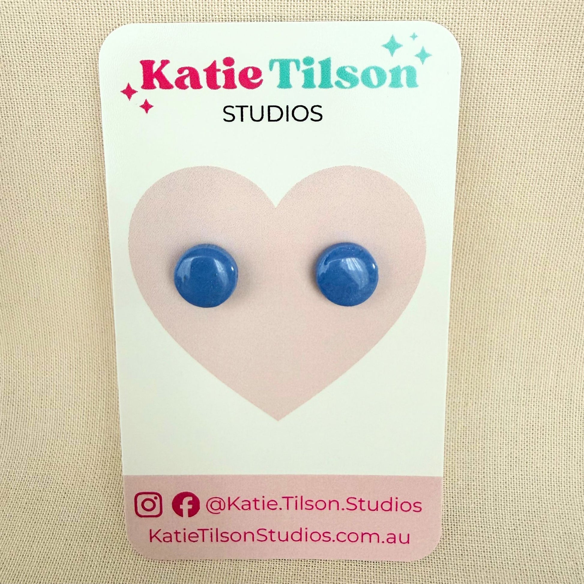 Cornflower blue circular stud earrings on a Katie Tilson Studios card against a beige background.