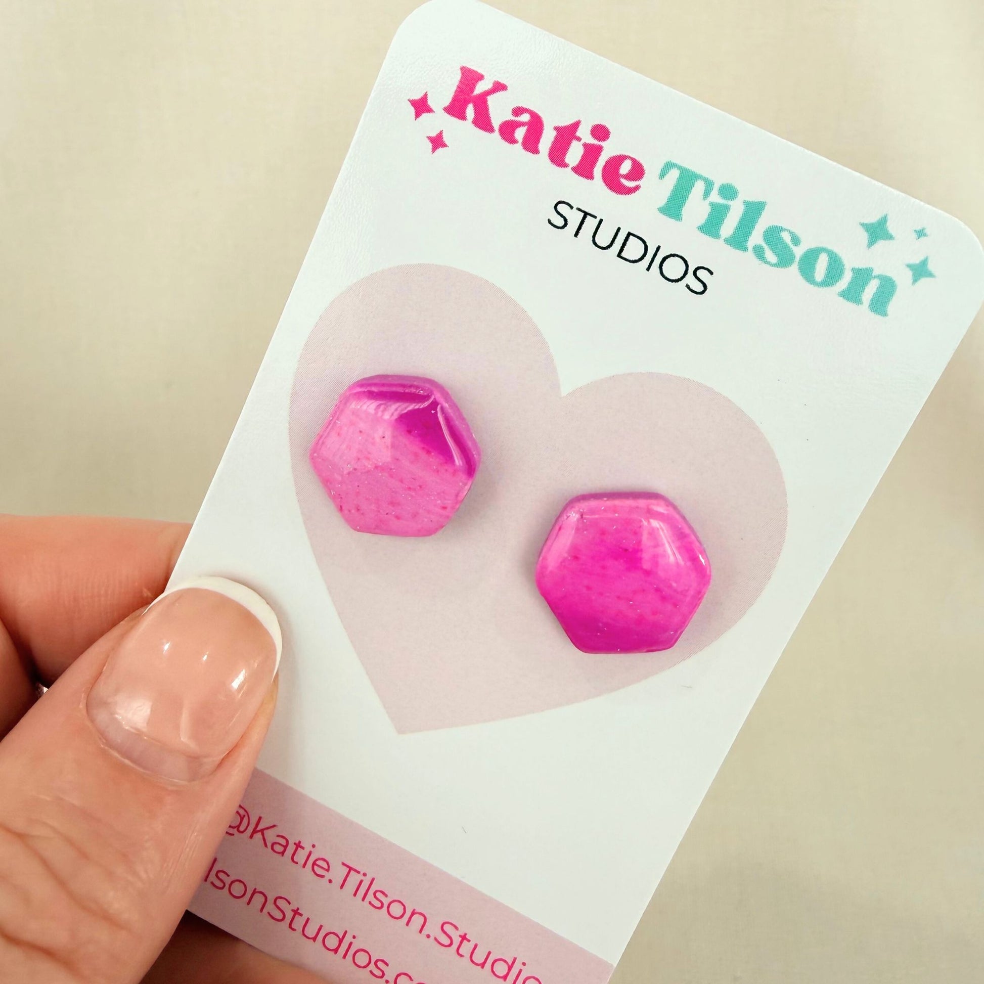Pink and purple geometric stud earrings on a Katie Tilson Studios card held by a hand.