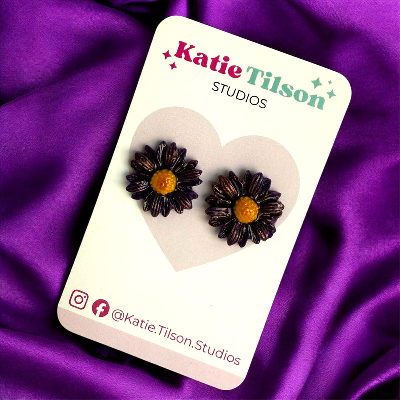 Flower-shaped earrings on a Katie Tilson Studios branded card against a purple satin background