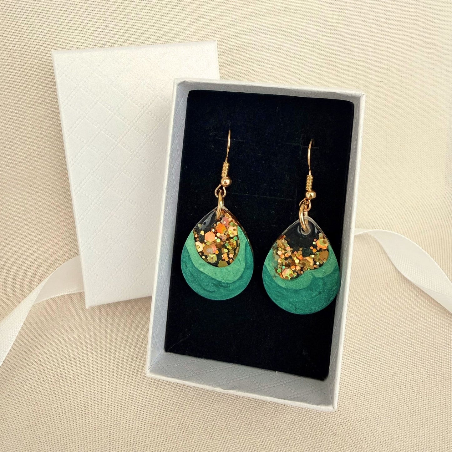 Emerald Geode handmade resin earrings in green and gold resting on black velvet insert in a white gift box.