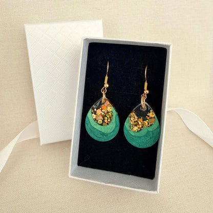 Emerald Geode handmade resin earrings in green and gold resting on black velvet insert in a white gift box.