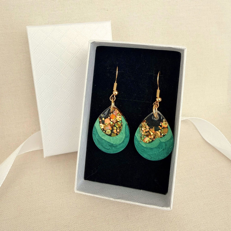 Emerald Geode handmade resin earrings in green and gold resting on black velvet insert in a white gift box.