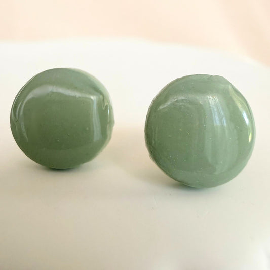 Glossy eucalyptus green stud earrings in a circular shape design resting on a white surface.