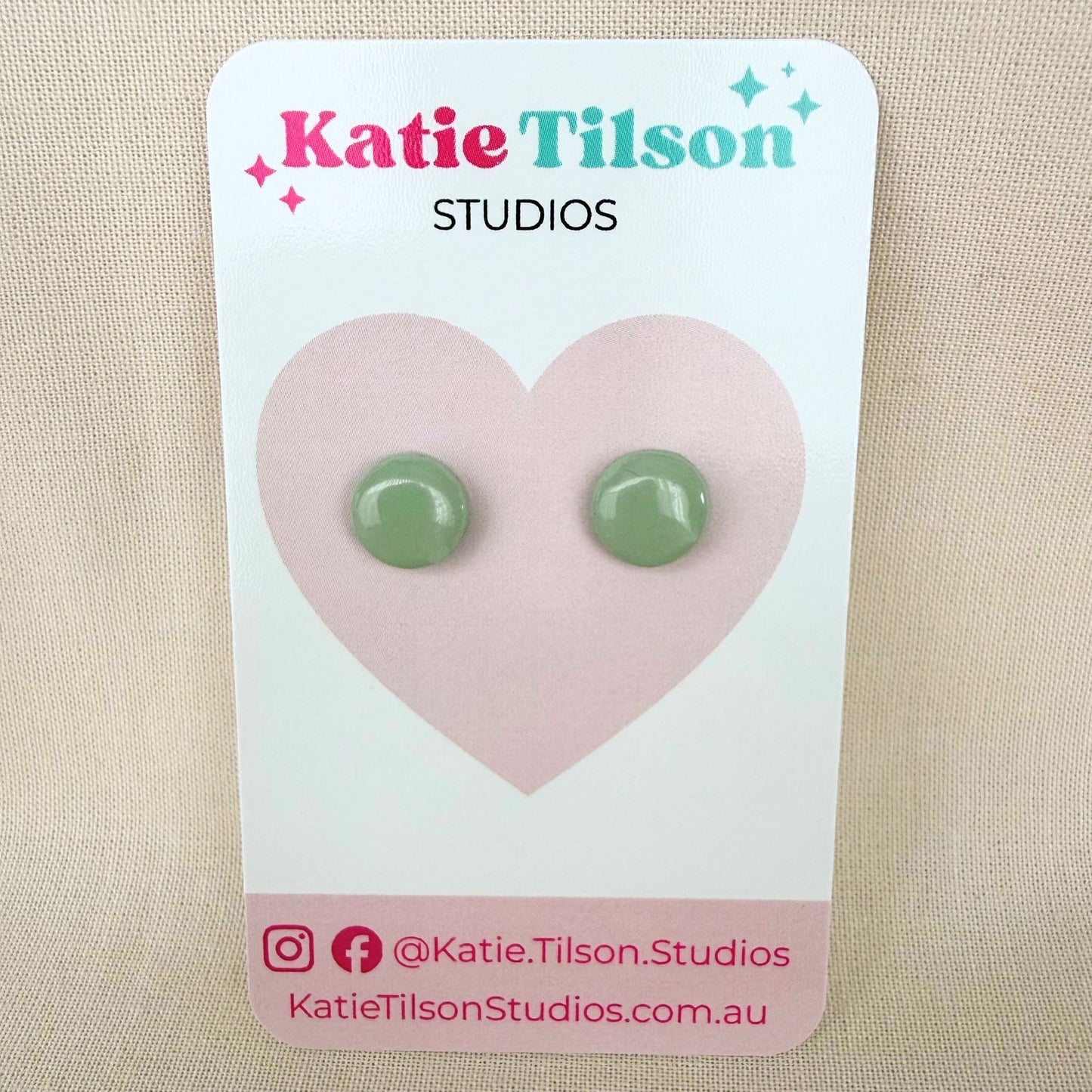 Eucalyptus green circular stud earrings on a Katie Tilson Studios branded earring card.