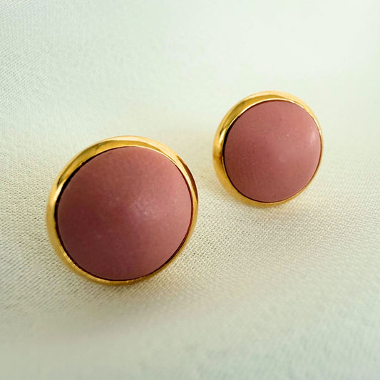 Close up of a pair of Everyday Stud earrings in domed shape, blush colour with gold bezel.