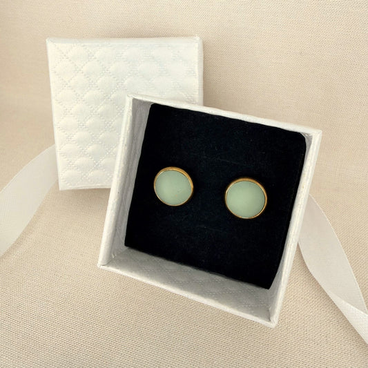 Pair of Australian handmade light eucalyptus green earrings with gold bezel in a white box on a beige background.
