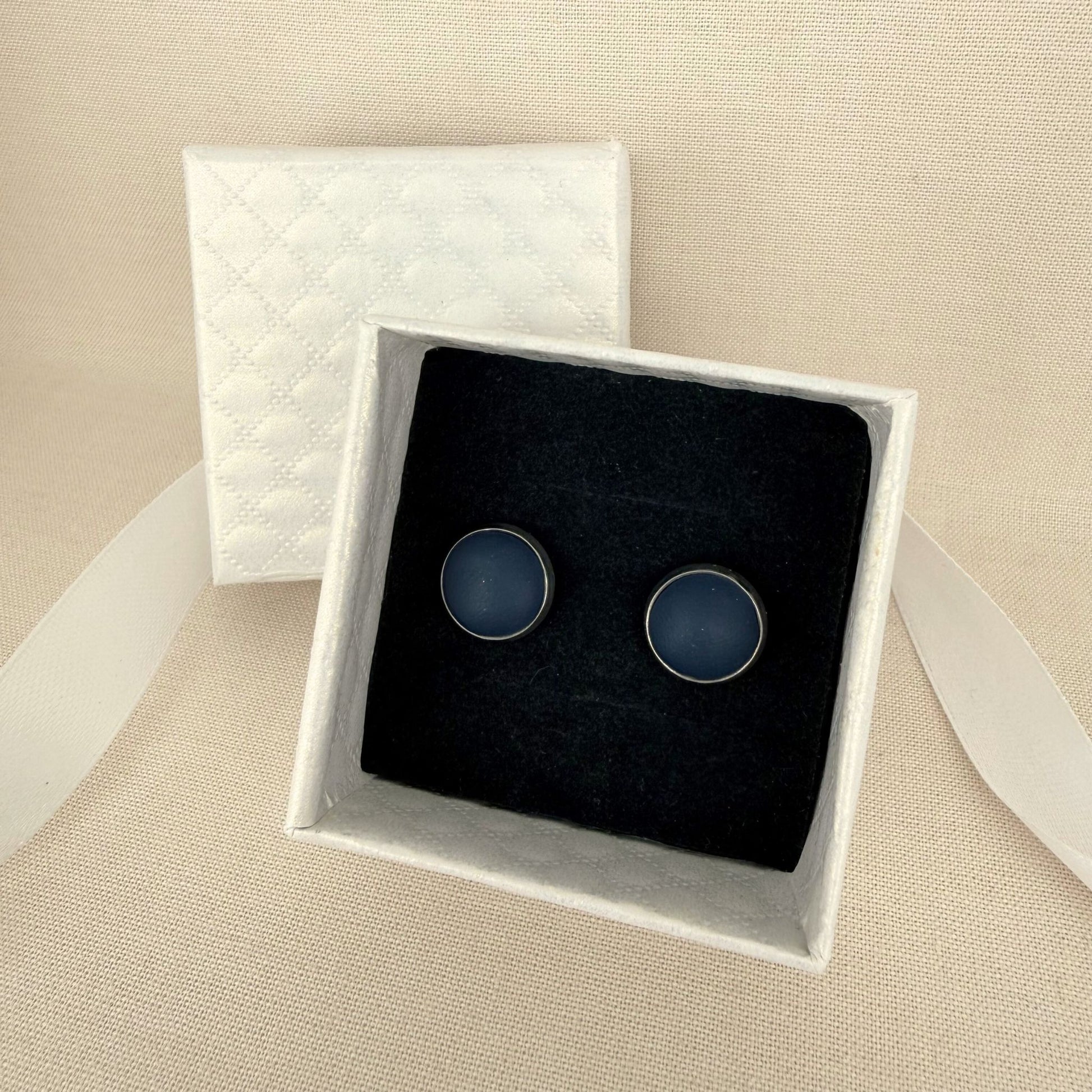 Pair of Australian handmade navy stud earrings with silver bezel in a white box on a beige background.