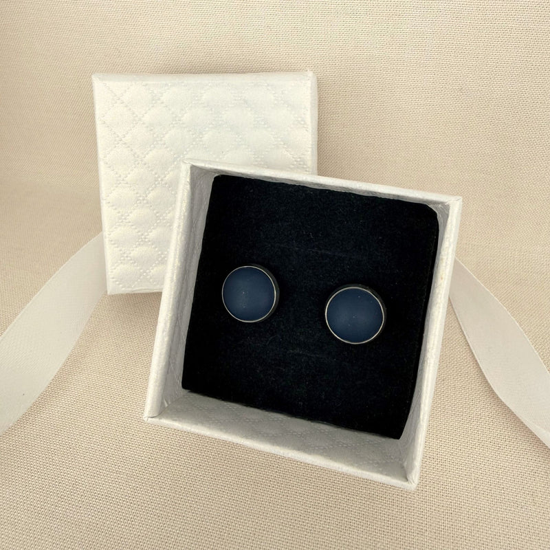 Pair of Australian handmade navy stud earrings with silver bezel in a white box on a beige background.