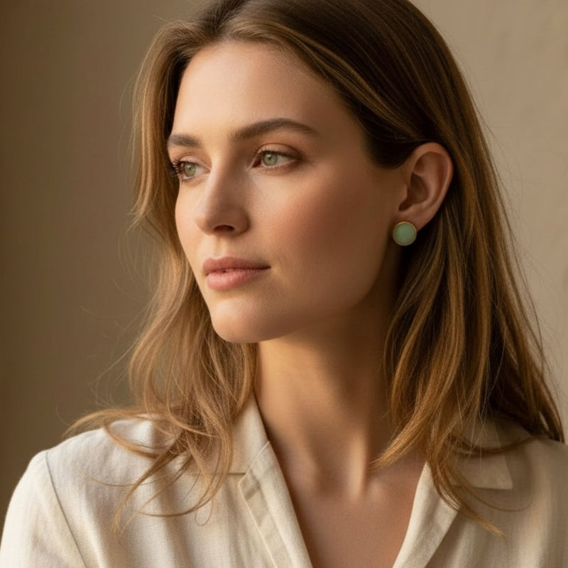 Woman wearing Australian handmade stud earrings in eucalyptus green with gold bezel against a neutral background.