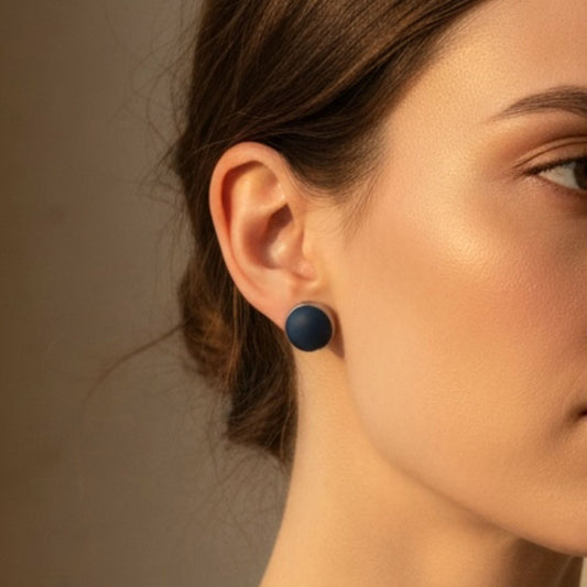 Close-up of a woman wearing a dark blue round stud earring set in a silver bezel against a neutral background.