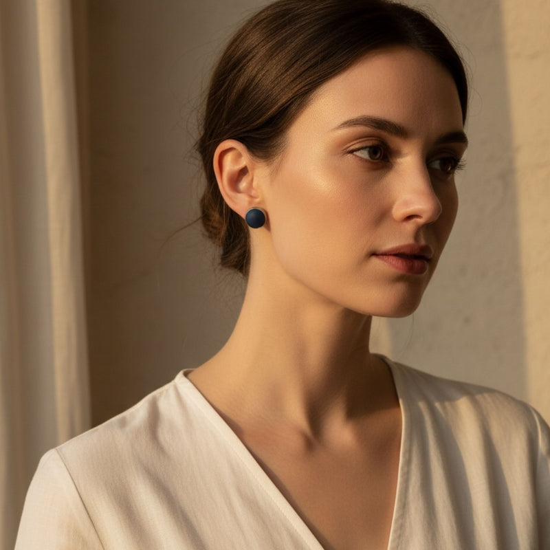 Woman wearing a deep navy stud earring with a silver bezel against a neutral background.
