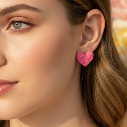 Close-up of a woman wearing pink polymer clay heart-shaped stud earrings with embossed floral details.