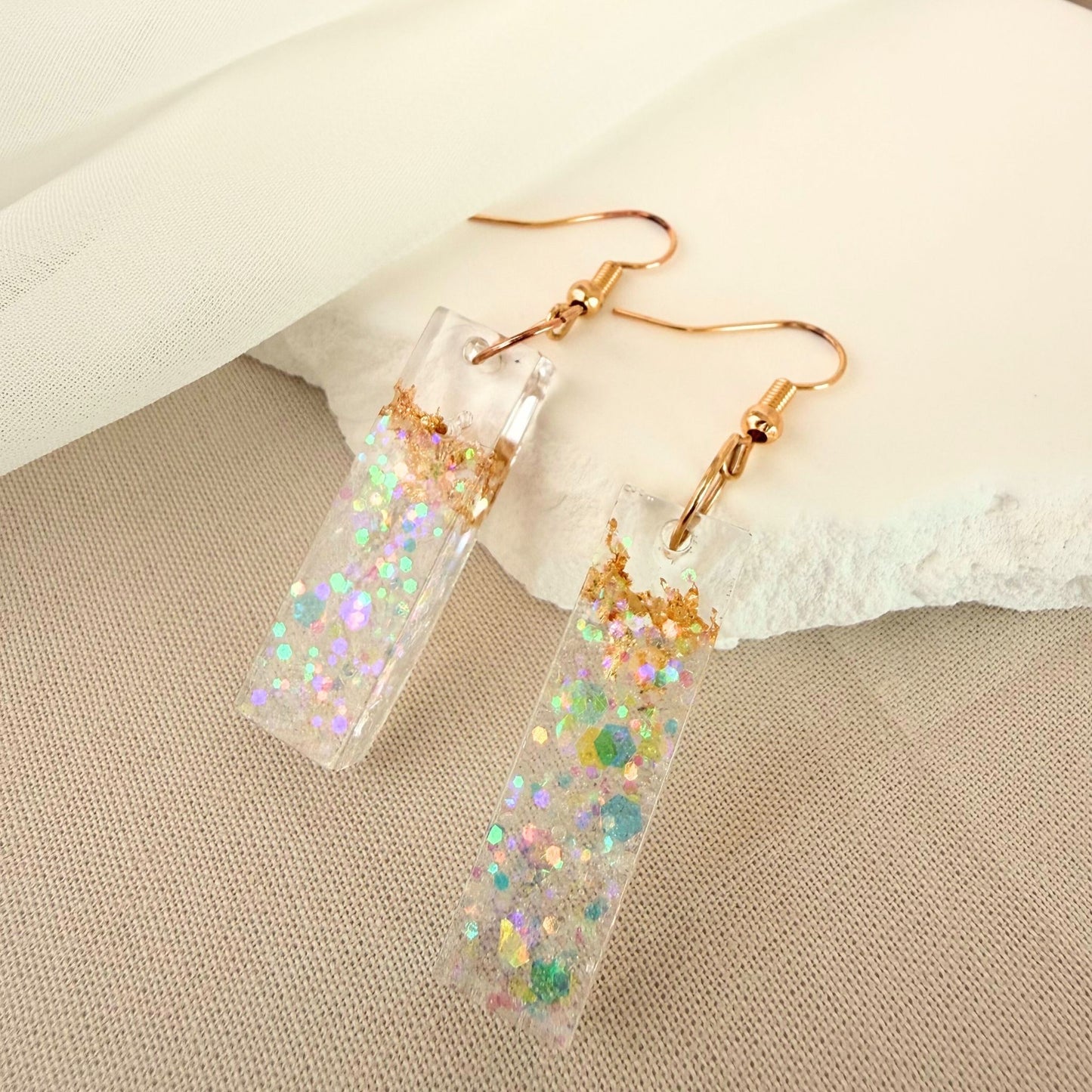Australian handmade dangle earrings Gilded Shore transparent resin with embedded gold leaf styled against a white rock. 