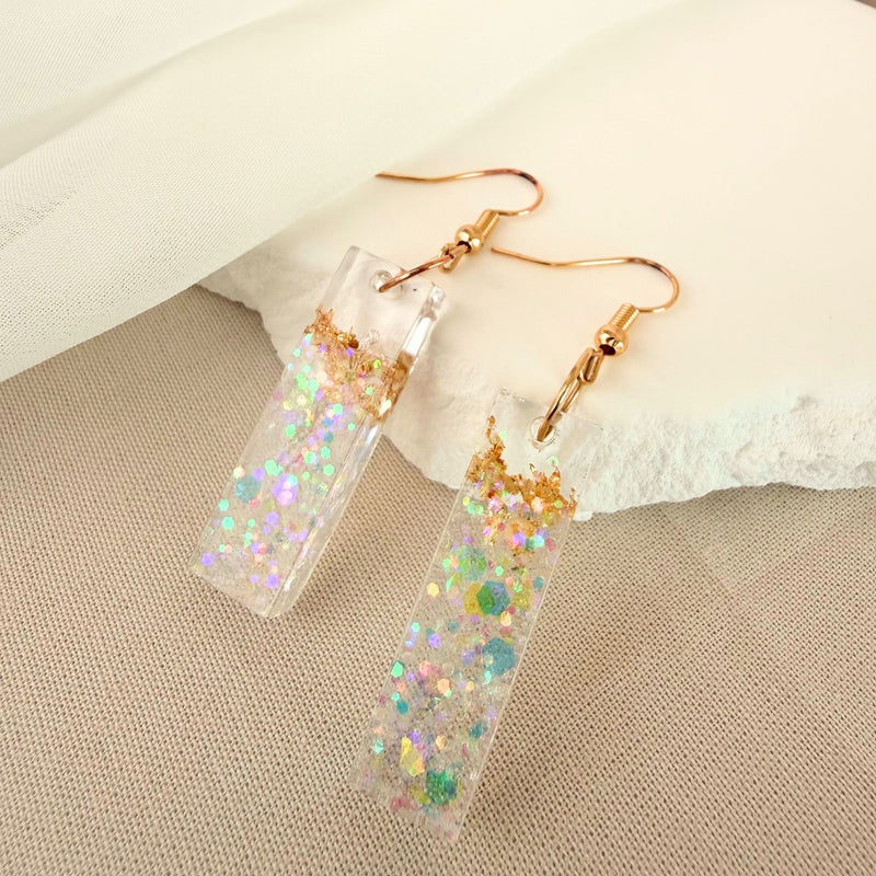 Australian handmade dangle earrings Gilded Shore transparent resin with embedded gold leaf styled against a white rock. 