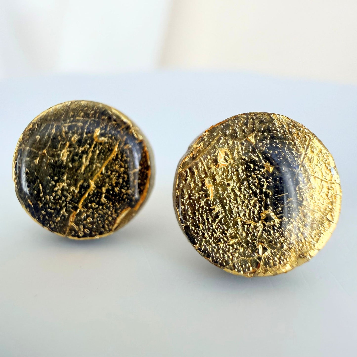 A pair of gold gilded circle studs with a glossy resin finish resting on a white surface.