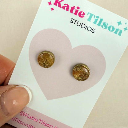 Gold round stud earrings on a Katie Tilson Studios card held by a hand.