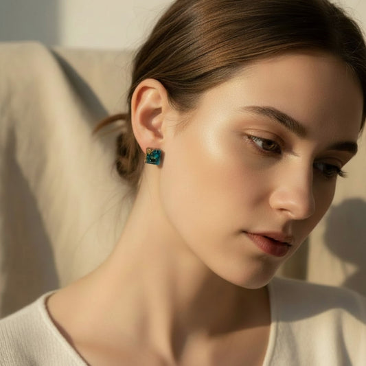 Australian handmade stud earrings Gilded Tide in teal resin with gold accents worn on ear by woman in beige setting.