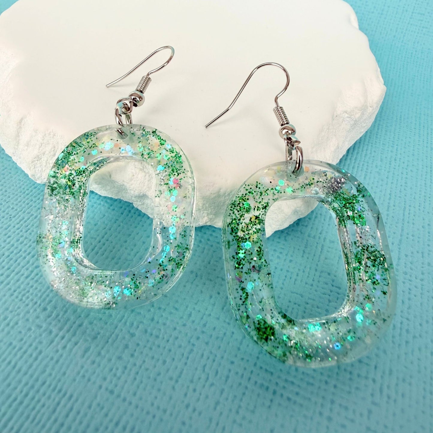 Green glittery hoop shaped handmade resin dangle earrings on a light blue background with a white stone.