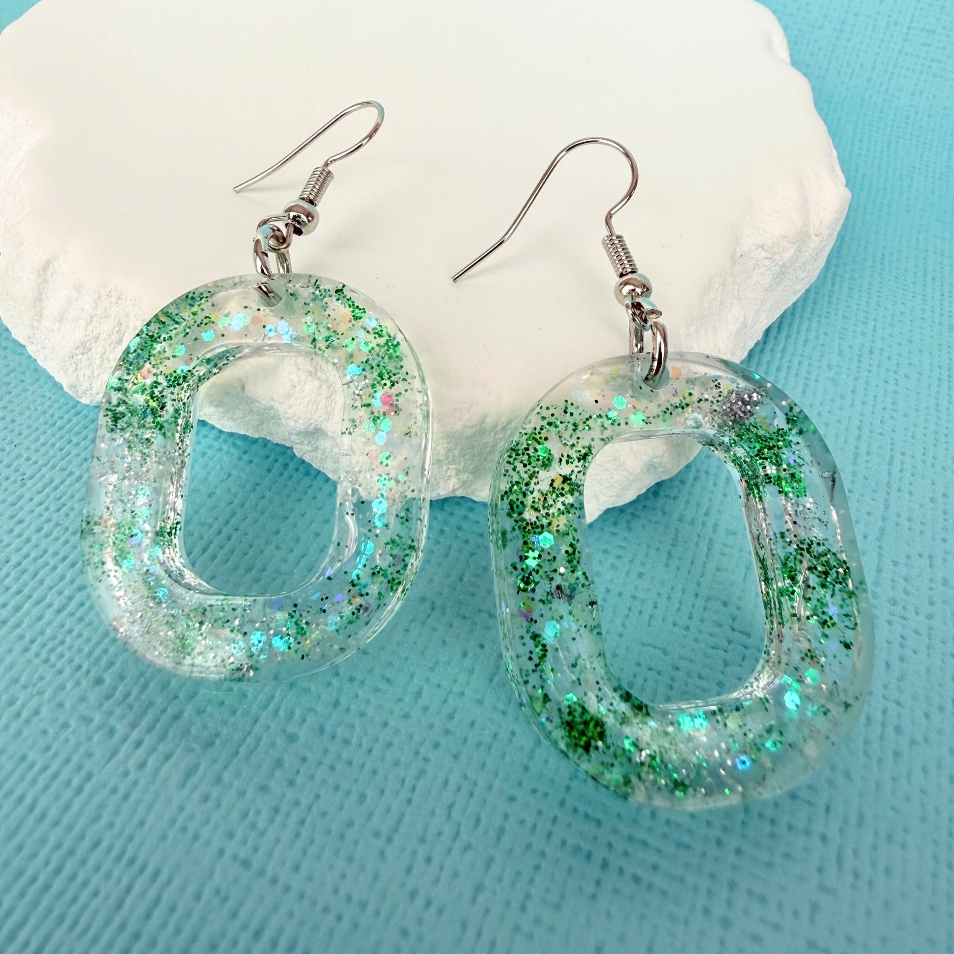 Green glittery hoop shaped handmade resin dangle earrings on a light blue background with a white stone.