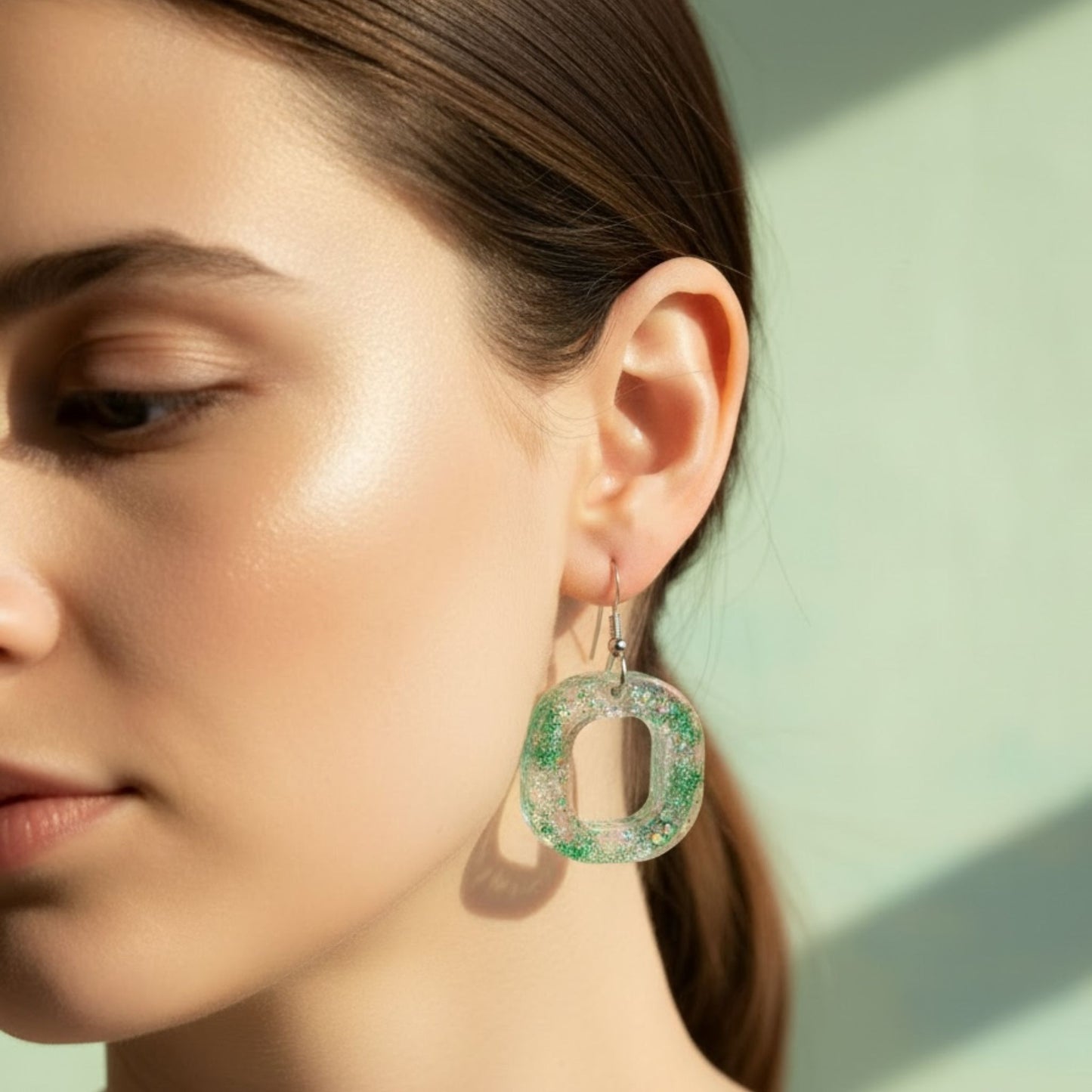 Australian handmade resin dangle earrings in oval shape with green sparkle worn on the ear.
