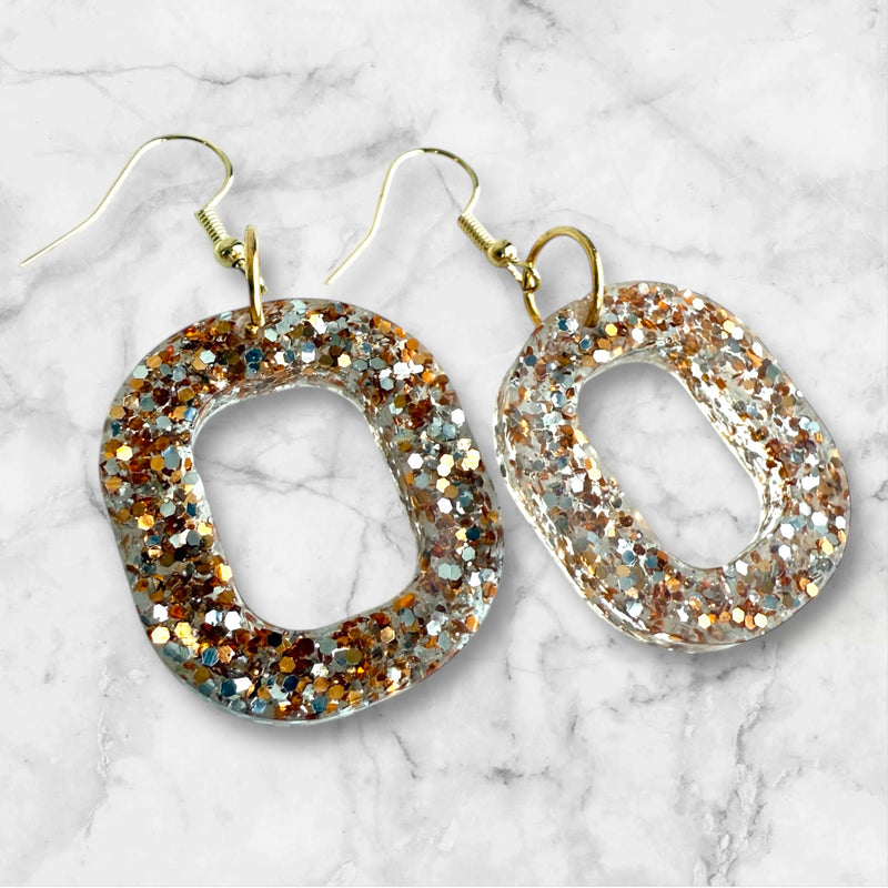 Circular resin glitter earrings with on a marble background