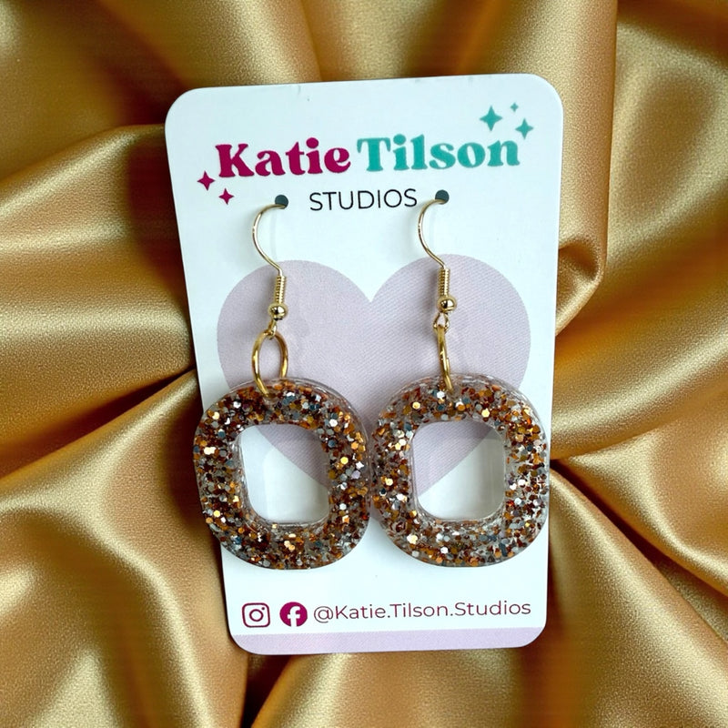 Katie Tilson Studios earrings on a display card with glittery gold circular earrings.