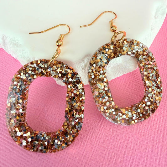 Glittery hoop shaped dangle earrings on a pink and white background.