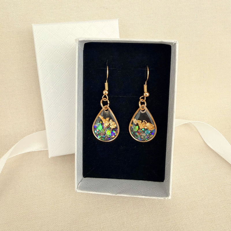Golden Light resin teardrop shaped earrings in transparent resin with gold leaf shimmer resting on a black velvet insert in a white gift box.