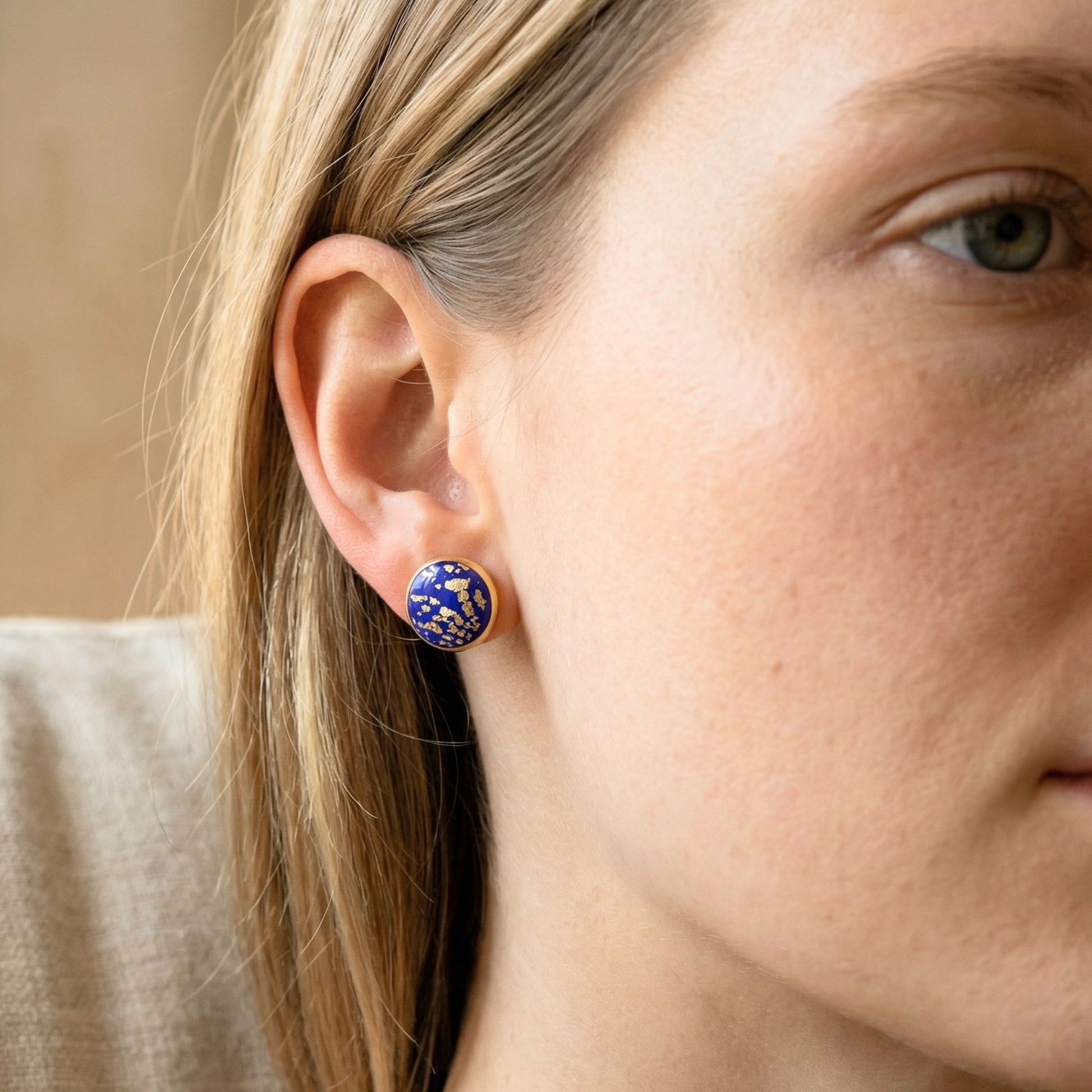 Good Vibes handmade stud earrings in a cobalt blue colour with gold flecks and gold bezel worn on woman's ear.