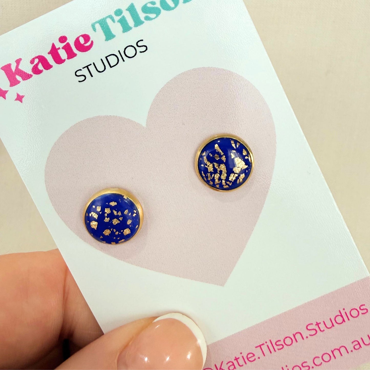 Cobalt blue and gold stud earrings on a Katie Tilson Studios card held by a hand.