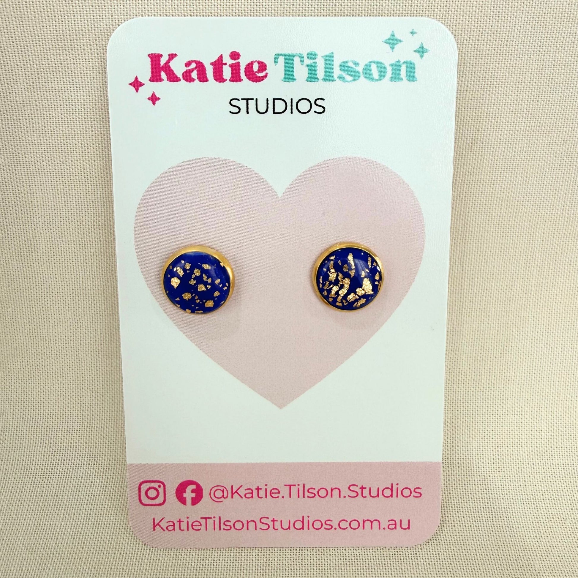 Pair of cobalt blue and gold earrings on a Katie Tilson Studios card against a beige background.