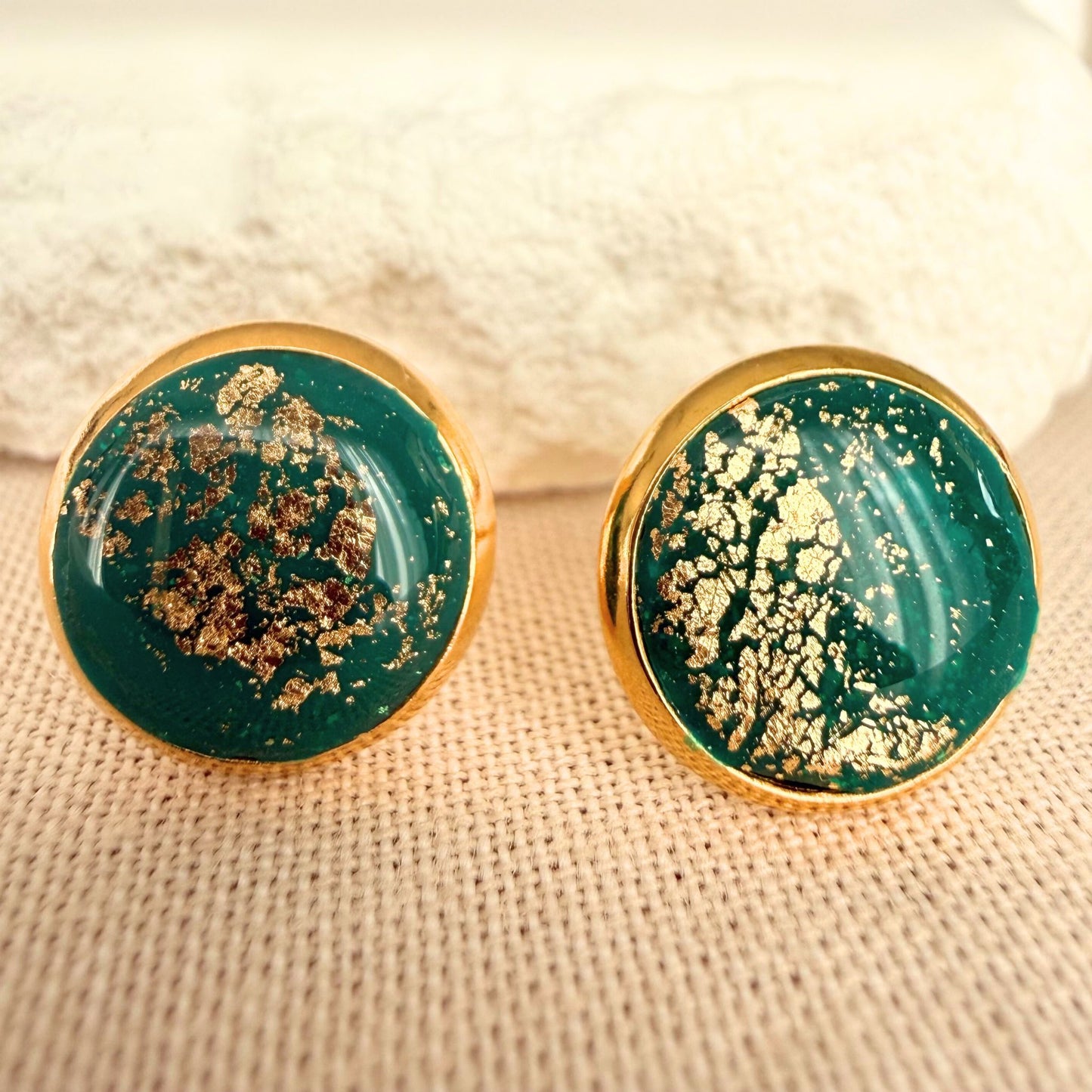 Emerald green round resin stud earrings with gold details and gold bezel on a beige surface.