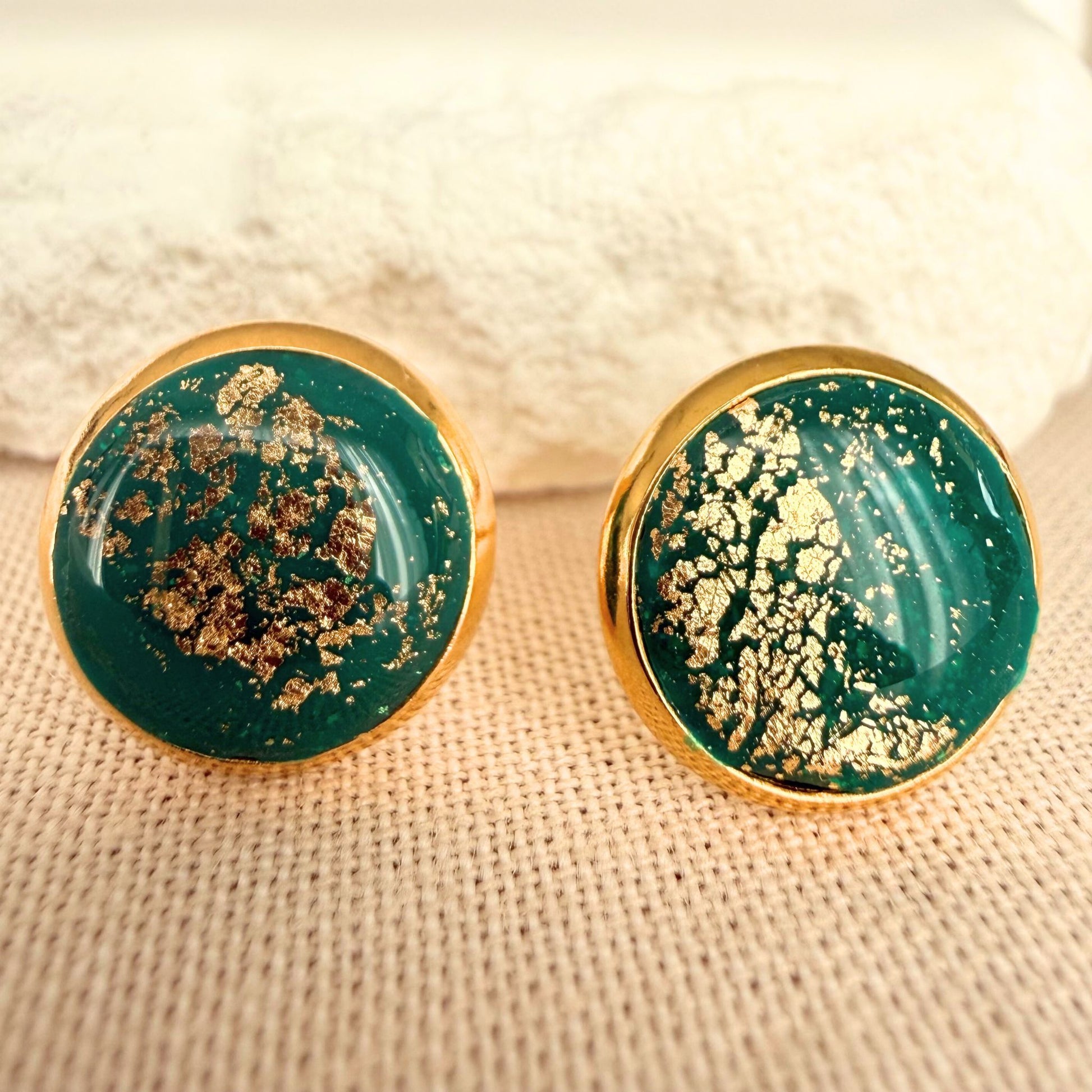Emerald green round resin stud earrings with gold details and gold bezel on a beige surface.