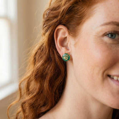 Close-up of a woman wearing green stud earrings with gold details.