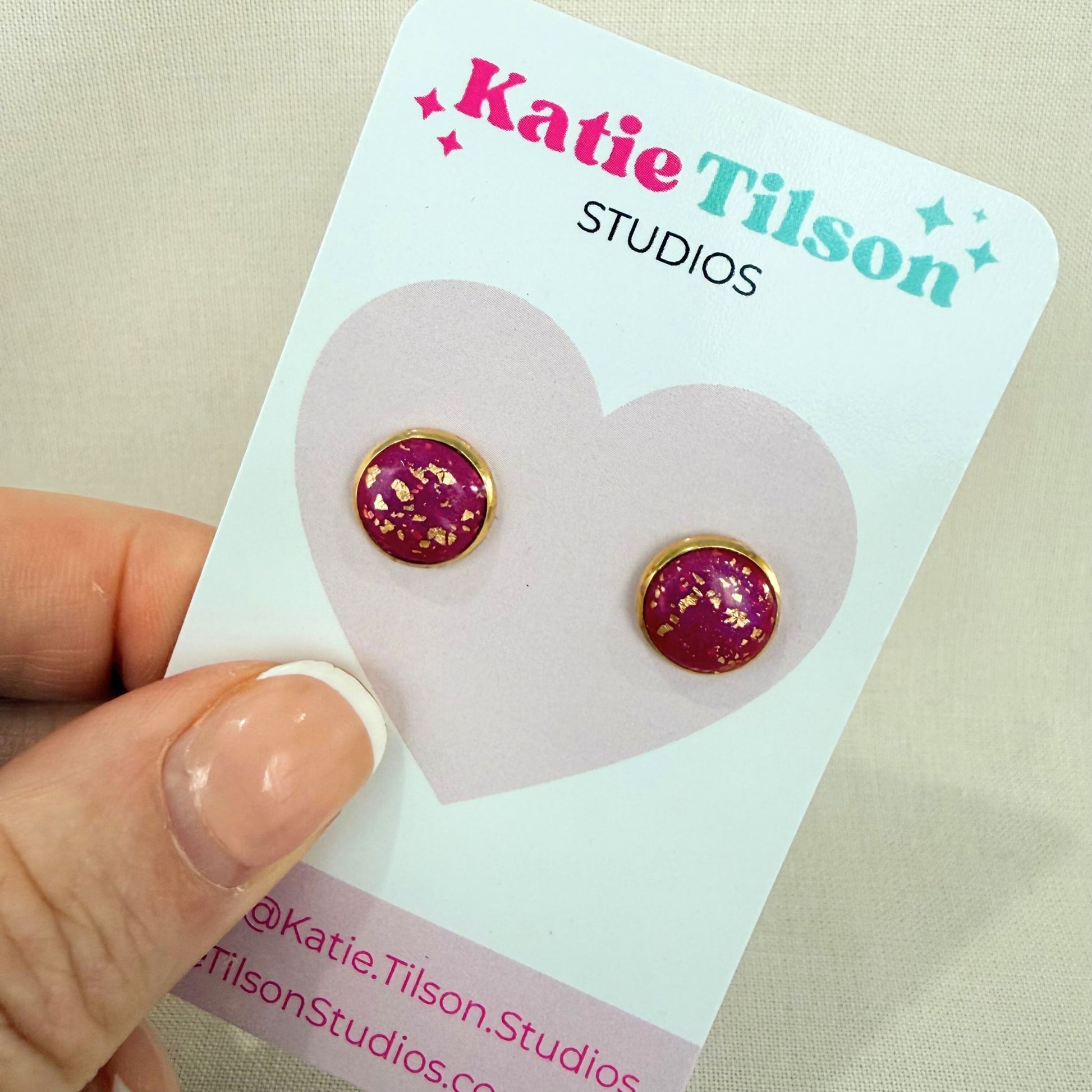 Magenta and gold earrings stud on a Katie Tilson Studios card held by a hand.